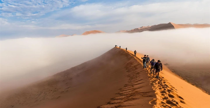 Tourists walk over sand dunes in the Namib desert