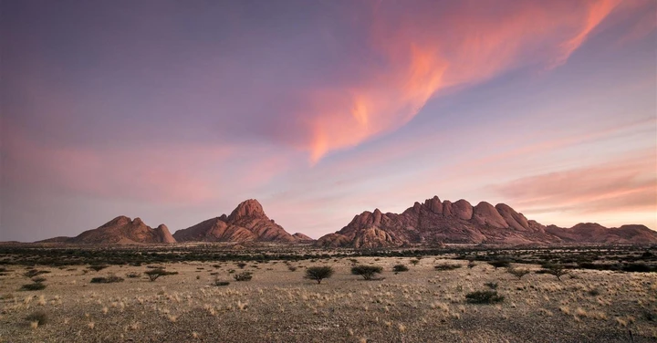 Céu cor de rosa serve de pano de fundo para os picos rochosos de Spitzkoppe durante o amanhecer